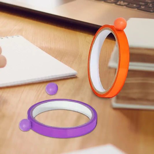 Two Sticky Toys for Kids—orange and purple wristbands, each with a matching sticky ball—rest on a desk near books and a laptop. These multifunctional sensory fidget toys offer stress relief and are perfect travel companions for all ages.