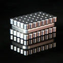 A Biscuits Fidget Slider, a rectangular metallic executive desk toy with a cartoon biscuit design and textured surface, sits on a reflective black surface—this rustproof sensory toy for kids originates from China.