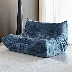 A modern Fireside Loveseat Sofa Couch in Chenille Blue with an ergonomic, curved, quilted design sits on a light rug in a contemporary room with neutral walls and sheer white curtains.