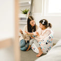 A woman and a young girl read together in a cozy, well-lit room; the girl sits comfortably in the Milano Kids Bean Bag Chair for Comfort and Fun, showcasing its versatile design and durable material.