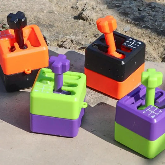 Four colorful Manual Gear Shifter Keychain 3D Printed Fidget Toys, shaped like miniature gear shifters, sit on a surface. Each chemical-free mood enhancer features a patterned stick shift top in orange, black, green, and purple. Made in Mainland China.
