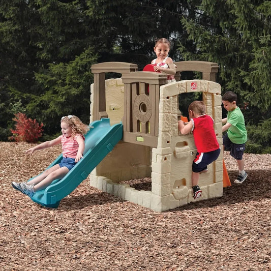 Four young children play outdoors on the Woodland Climber II Kids Playset for Ages 2 to 6 Years. One girl slides down the toddler slide, while others climb and explore, surrounded by trees and wood chips.