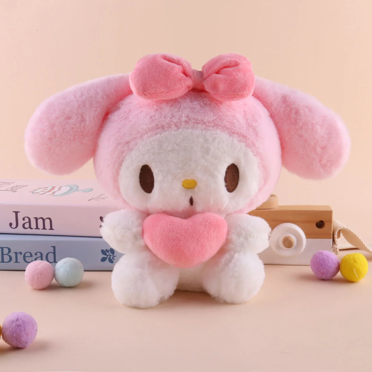 A 22cm Sanrio Hello Kitty Kuromi Pillow KT Plush Toy in Melody color, shaped as a soft stuffed animal, sits by pastel books and colorful pom-poms—a cute gift for girls and a delight for any plush toy lover.