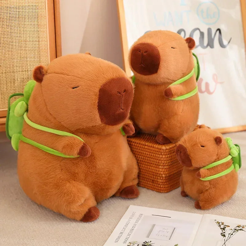 Three Cute Turtle Backpack Capibara Strawberry Hat Capybara Plush Toys in different sizes are displayed on a table with decor and a framed picture in the background.