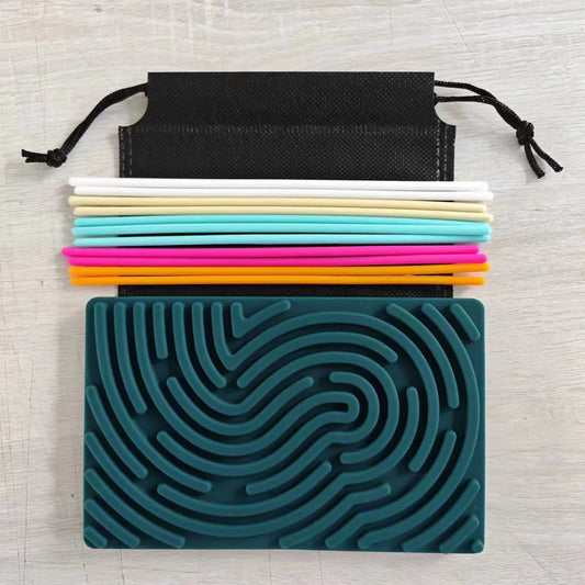 A Children’s Puzzle Silicone Sensory Activity Board (food grade, BPA free) with textured teal grooves is placed below colorful silicone drinking straws and a black drawstring pouch on a light wooden surface.