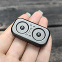 A close-up of a hand holding the Owl Push Slider Fidget Toy, an adult metal finger push spinner with two circular indents and raised shapes, used for decompression and haptic feedback, resembling EDC gear.