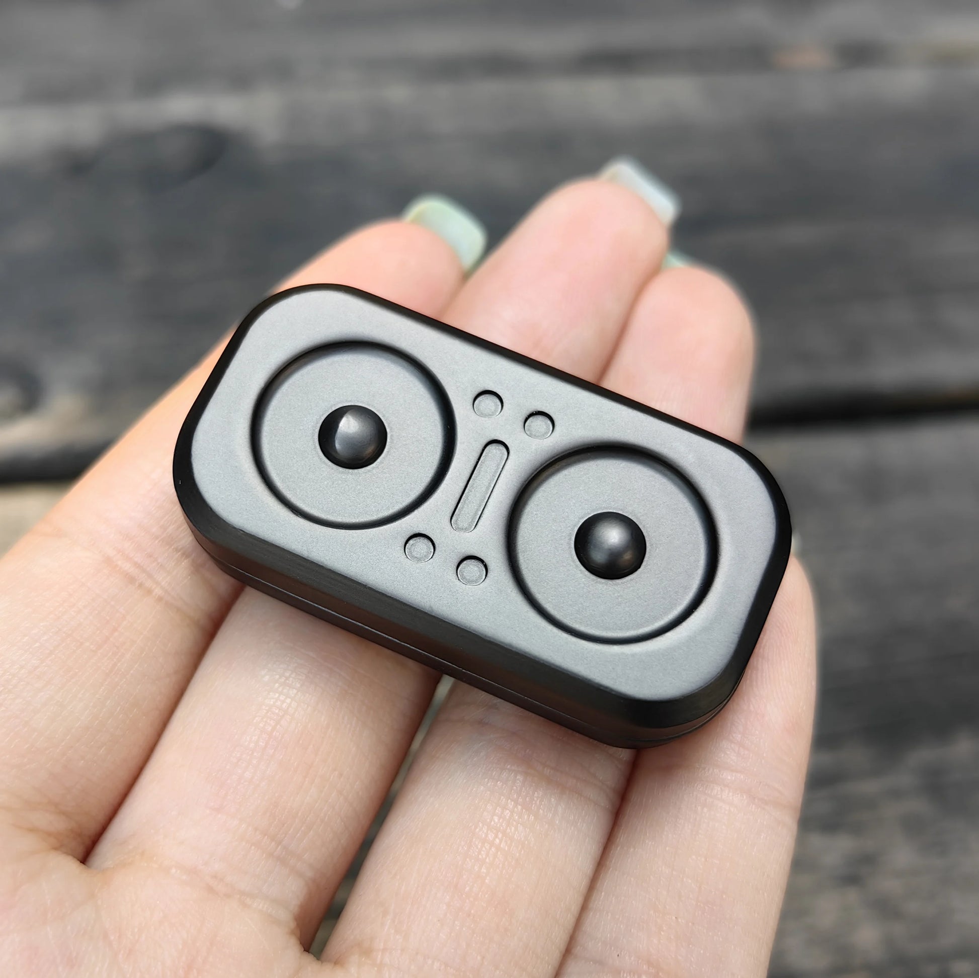 A close-up of a hand holding the Owl Push Slider Fidget Toy, an adult metal finger push spinner with two circular indents and raised shapes, used for decompression and haptic feedback, resembling EDC gear.