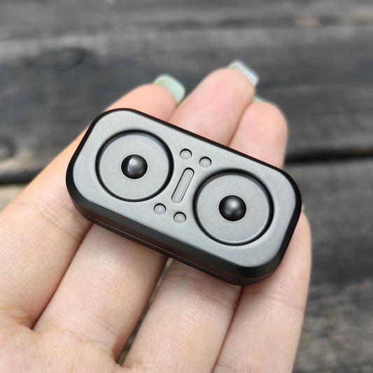 A close-up of a hand holding the Owl Push Slider Fidget Toy, an adult metal finger push spinner with two circular indents and raised shapes, used for decompression and haptic feedback, resembling EDC gear.