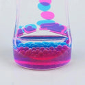 A close-up of the Liquid Motion Bubbler Timer shows pink and blue bubbles in clear liquid inside a transparent container, ideal for sensory activity, anxiety relief, or autism support, set against a light gray background.