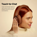 A woman with long red hair wears Edifier ES850NB Wireless Headphones, touching the right ear cup to use the Touch-to-Chat feature, which lets in ambient sound even when noise cancelling is on.
