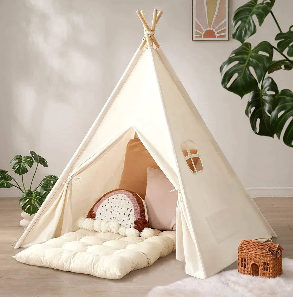 Cream-colored teepee play tent with a Thick Padded Play Cushion, decorative pillows, and a small woven house-shaped basket.