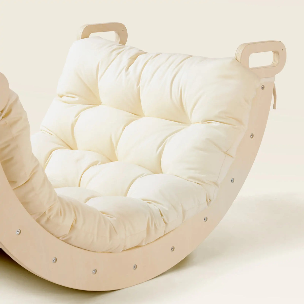 A Thick Padded Play Cushion in a tufted cream color, fitted onto a curved wooden rocker with handles on both ends.