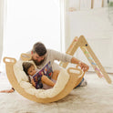 A father reads a storybook to his daughter, who is resting inside a curved wooden rocker lined with a Thick Padded Play Cushion.