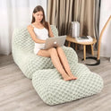 A woman relaxes on a Widen-Green Bean Bag Sofa Chair with matching footstool, using her laptop indoors by a window with curtains. A small round table with books sits beside this comfy modern lounge chair for living room or bedroom.