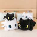 Four 30cm and 40cm Plush Dragon Toys—Kawaii white and black dinosaur stuffed animals for boys and girls birthday gifts—are stacked in pairs on a bed with pale blue pillows and a wooden headboard behind.