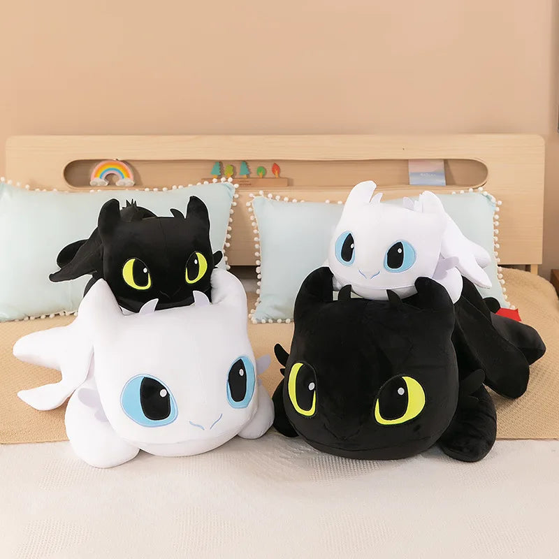 Four 30cm and 40cm Plush Dragon Toys—Kawaii white and black dinosaur stuffed animals for boys and girls birthday gifts—are stacked in pairs on a bed with pale blue pillows and a wooden headboard behind.