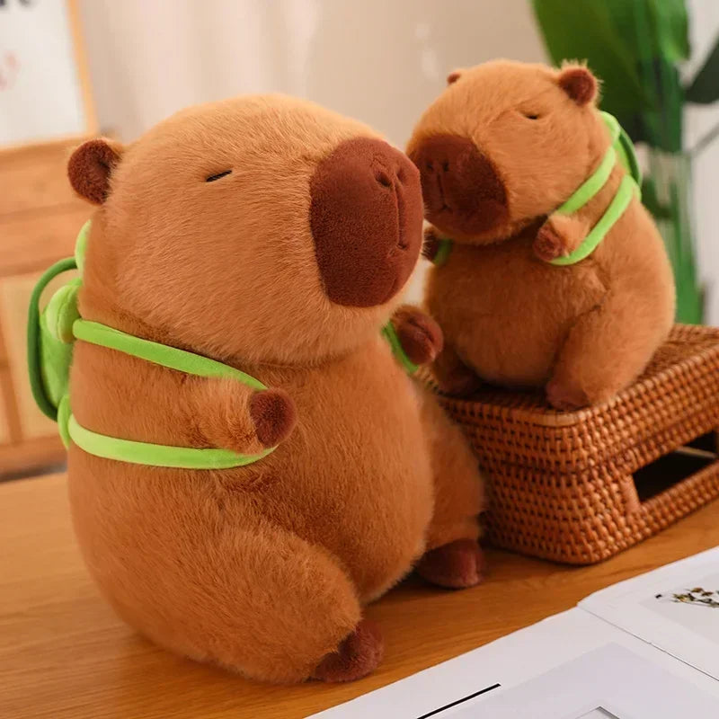 Two Cute Turtle Backpack Capibara Strawberry Hat Capybara Plush Toy Stuffed Animals sit on a wooden surface, one on a wicker box and the other on the table. Both soft dolls look relaxed and content—perfect as kids toys or birthday gifts.