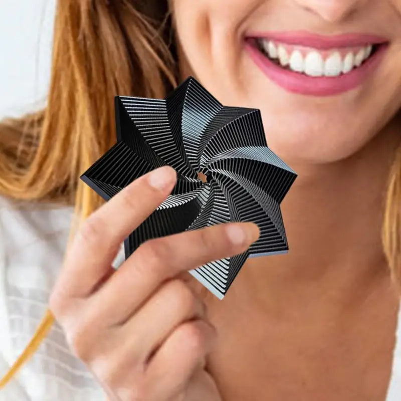 A smiling person from Mainland China holds a black Fidget 3D Spinner Stress Relief Toy with geometric lines and pointed edges, made of durable rubber, near their face.