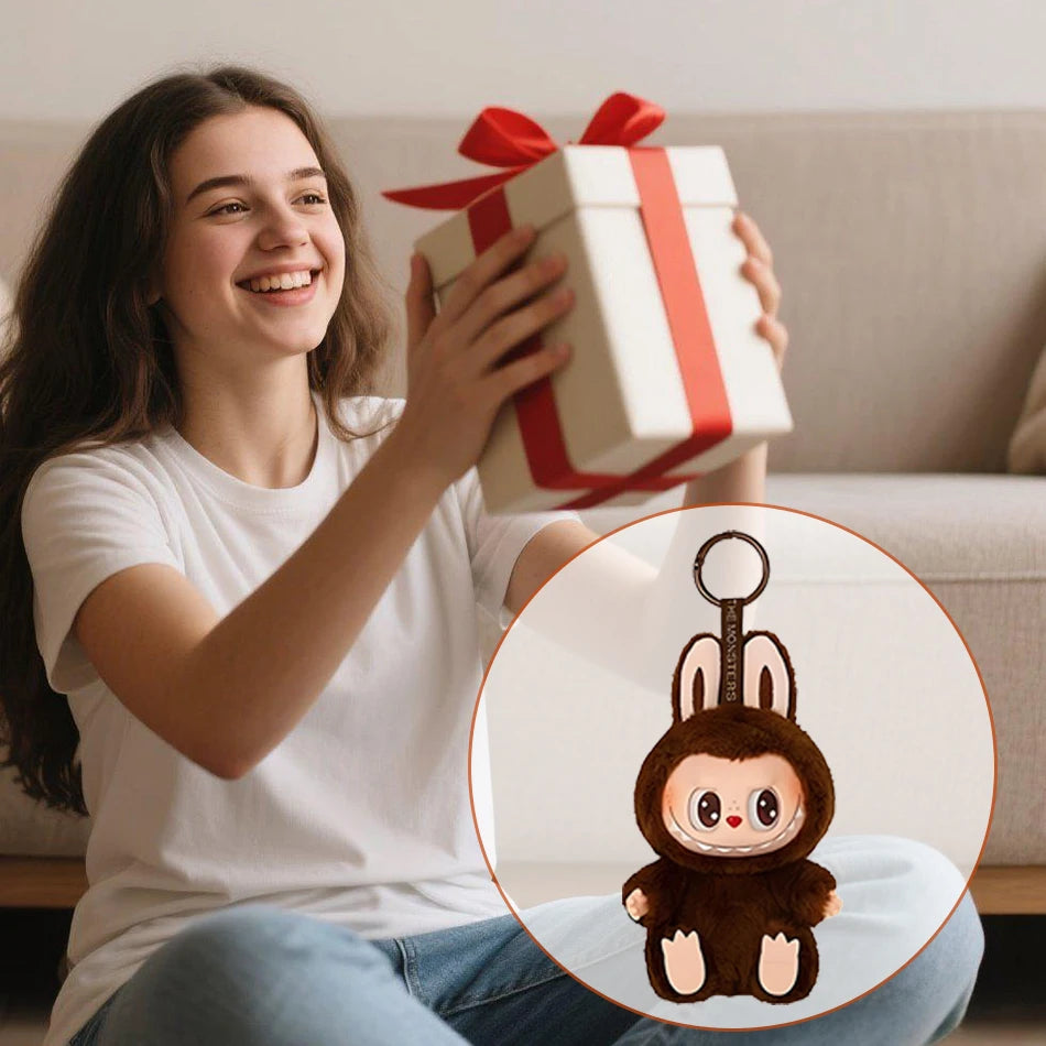 A smiling girl sits on the floor holding a wrapped gift with a red ribbon. An inset shows a Cute Labubu The Monsters Box Toy Sweetheart vinyl doll keychain, shaped like an adorable animal in a brown bunny costume.