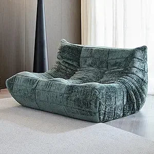 A modern Fireside Loveseat Sofa Couch in chenille green with ergonomic, deep cushioned seats rests on a light rug in a minimalist room featuring wood-paneled walls and sheer curtains.