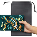 A hand holds a green Childrens Puzzle Silicone Sensory Activity Board made of food grade, BPA-free silicone, with colorful winding tracks. A textured black drawstring pouch is shown in the background.