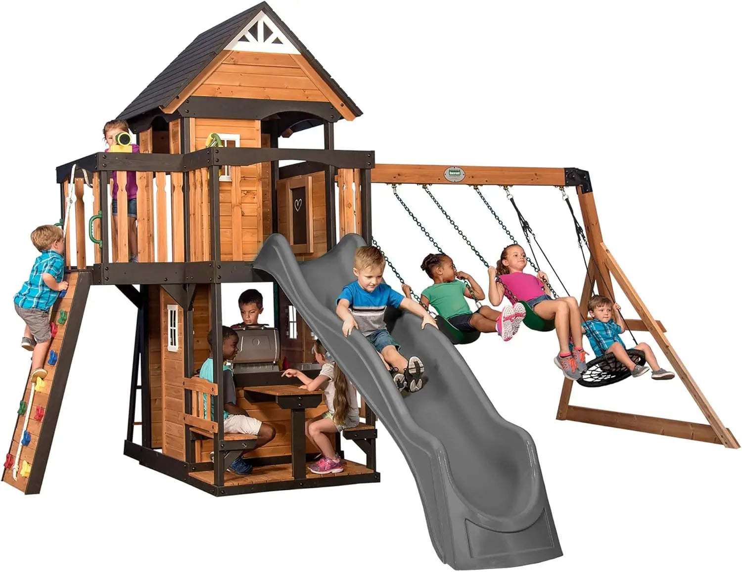Children play on the Playhouse Backyard Discovery Canyon Creek Cedar Swing Set with a grey slide, swings, climbing wall, clubhouse, and picnic table. Some kids swing, slide, and climb together outdoors enjoying this fun playset.