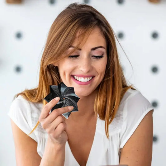 A woman with long brown hair and a white shirt smiles while holding a Fidget 3D Spinner Stress Relief Toy, featuring a geometric illusion design. The background is softly blurred with circular patterns.