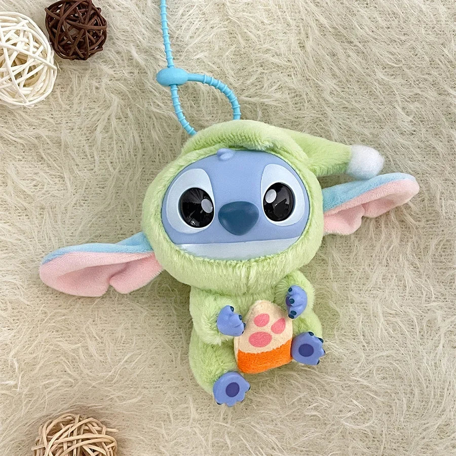 The Kawaii Accessories Stitch Plush Toy Lilo and Stitch Keychain features Stitch in a green onesie with a hood, holding a toy. This cute Eat Something Before Sleep Series backpack pendant is shown on a beige surface with decorative balls.