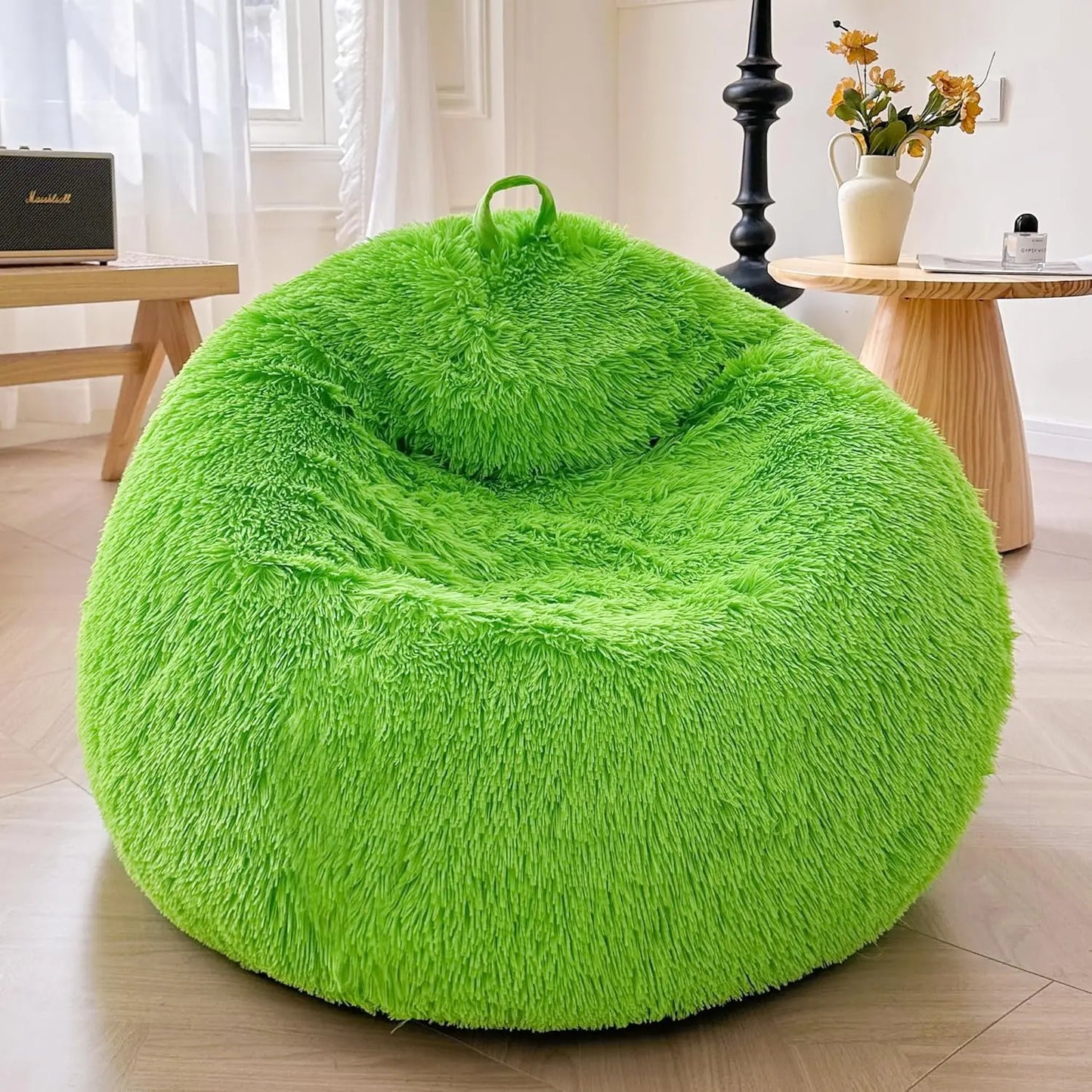 A lime green Faux Fur Comfy Bean Bag Cover (no filler) is in a cozy, sunlit room with a wooden side table, black floor lamp, and a vase of yellow flowers on another nearby table.