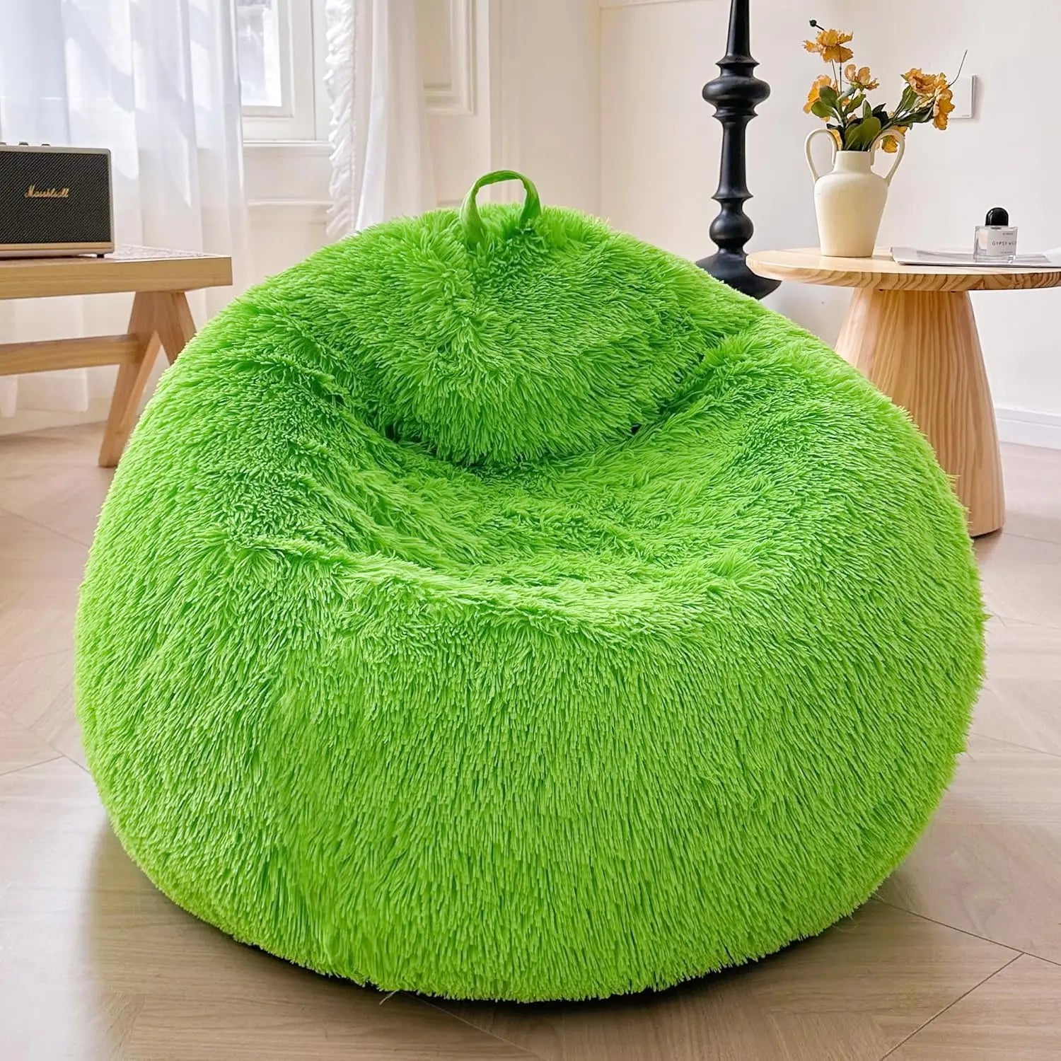 A lime green Faux Fur Comfy Bean Bag Cover (no filler) is in a cozy, sunlit room with a wooden side table, black floor lamp, and a vase of yellow flowers on another nearby table.