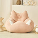 A Premium Teddy Velvet Bean Bag Sofa Cover in pink, featuring white ear-like details and extra storage for plush toys, adds a soft touch to a cozy room with minimalist decor and a small side table.