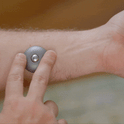 A person presses an ONO Scroller Titanium—small, round, and gray—against the inside of their arm, showing how it works on bare skin.