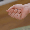 A hand repeatedly squeezes the ONO Scroller Titanium, a small gray fidget stress ball, demonstrating how it changes shape under pressure from the fingers.