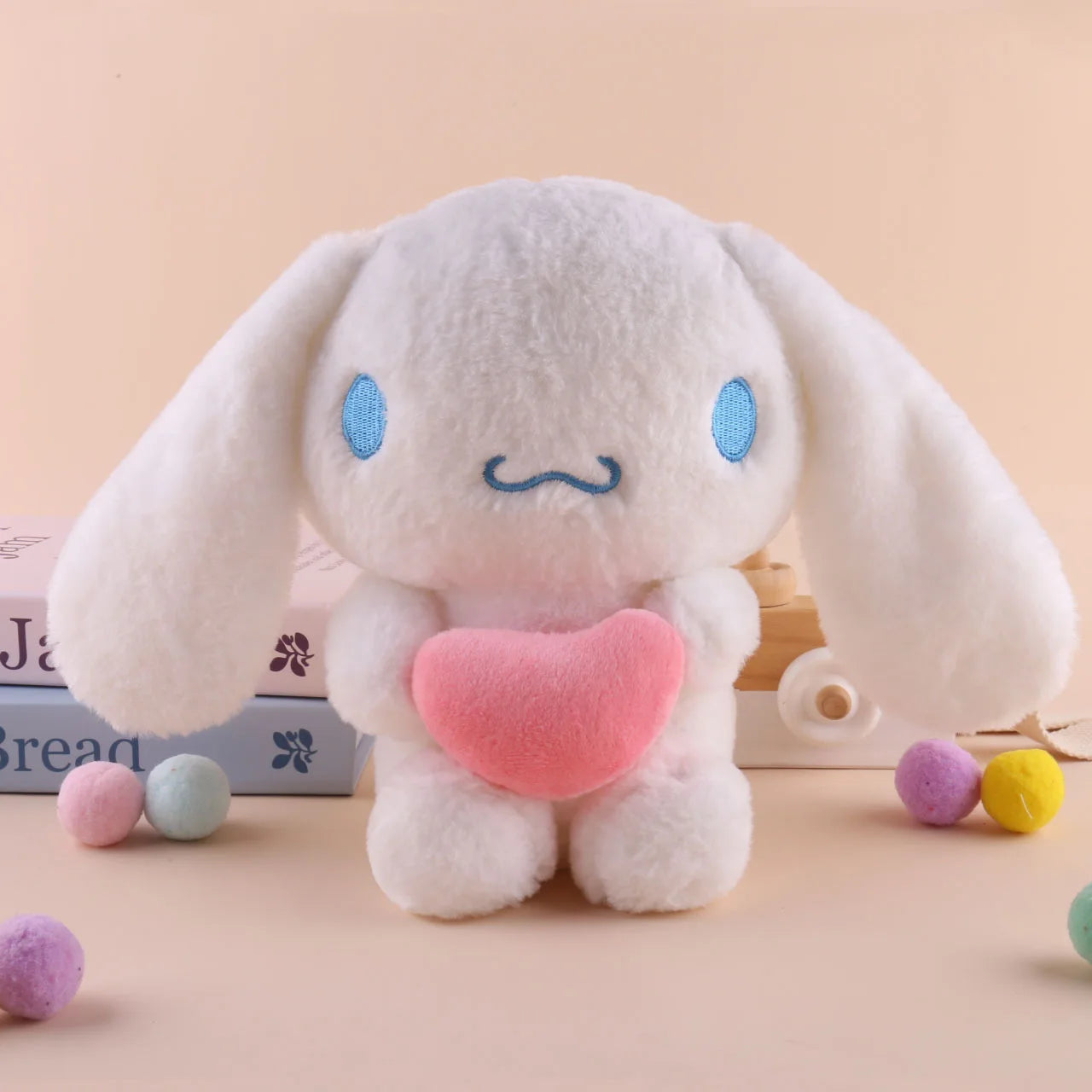 A 22cm Sanrio Hello Kitty Kuromi Pillow KT Plush Toy in Cinnamoroll color sits upright holding a pink heart, with colorful soft balls and books in the background on a light beige surface. Perfect soft stuffed animal gift for girls.