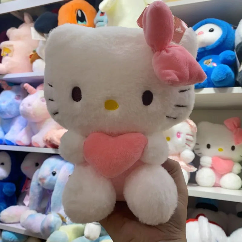 A hand holds the 22cm Sanrio Hello Kitty Kuromi Pillow KT Plush Toy, a soft stuffed animal gift for girls with a pink bow and heart, surrounded by other Sanrio plush toys on shelves in the background.