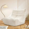 A modern, white Fireside Chair Bean Bag for adults sits on a wooden floor near a curved floor lamp. Sunlight streams through vertical blinds, casting shadows across the minimalistic, cozy room.