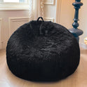 A black Faux Fur Comfy Bean Bag Cover (no filler) sits on a wooden floor by a window with white curtains, next to a tall, dark blue lamp.