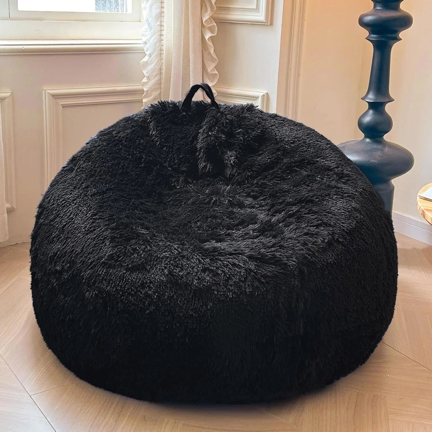 A black Faux Fur Comfy Bean Bag Cover (no filler) sits on a wooden floor by a window with white curtains, next to a tall, dark blue lamp.