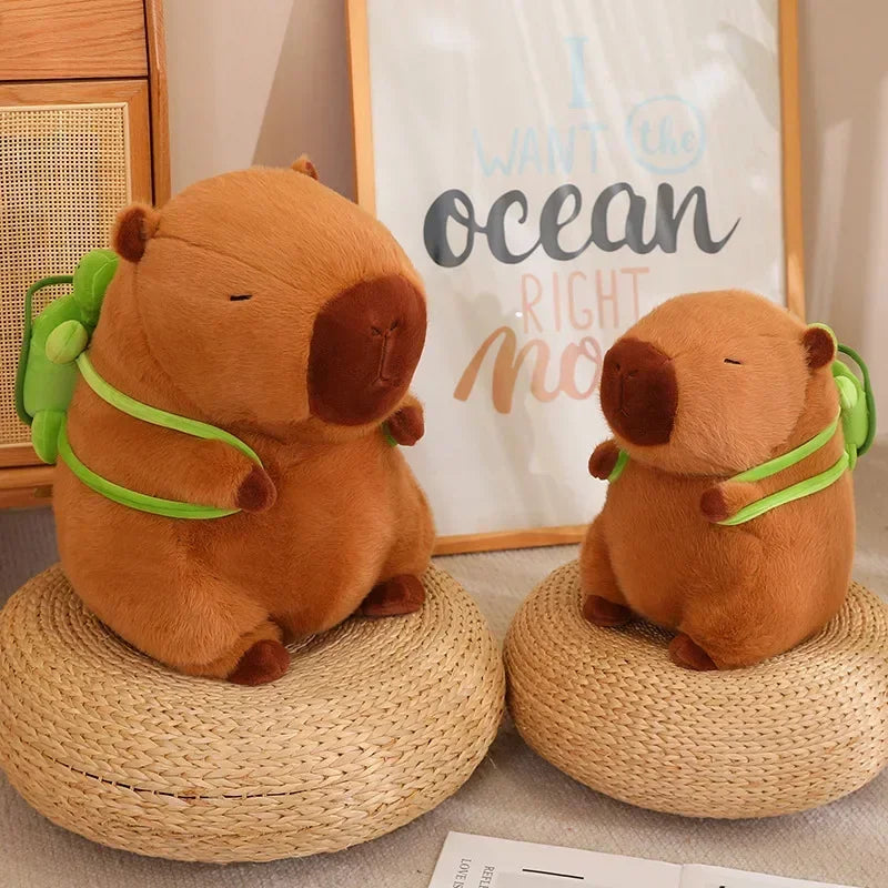 Two Cute Turtle Backpack Capybara Plush Toys with strawberry hats sit on woven mats next to a plush rabbit. Behind them, a framed I want the ocean right now print adds to the cozy, neatly arranged display.