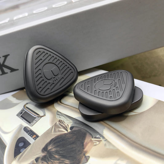 Two matte black EDC Fingertip Toys with a triangular, textured design and logo sit on an open magazine and in front of a book. These magnetic metal fidget sliders, made in Mainland China, feature a subtle metal accent for modern decompression.