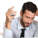 A man in a dress shirt and tie looks stressed at his desk, holding his head while fidgeting with a Biscuits Fidget Slider—an executive biscuit-design sensory toy—for stress relief.