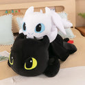 Two 30cm and 40cm Kawaii White and Black Plush Dragon Dinosaur Toys are stacked on a bed with pillows and a wooden headboard. Each plush is stuffed with soft PP cotton, making them perfect birthday gifts for boys and girls.