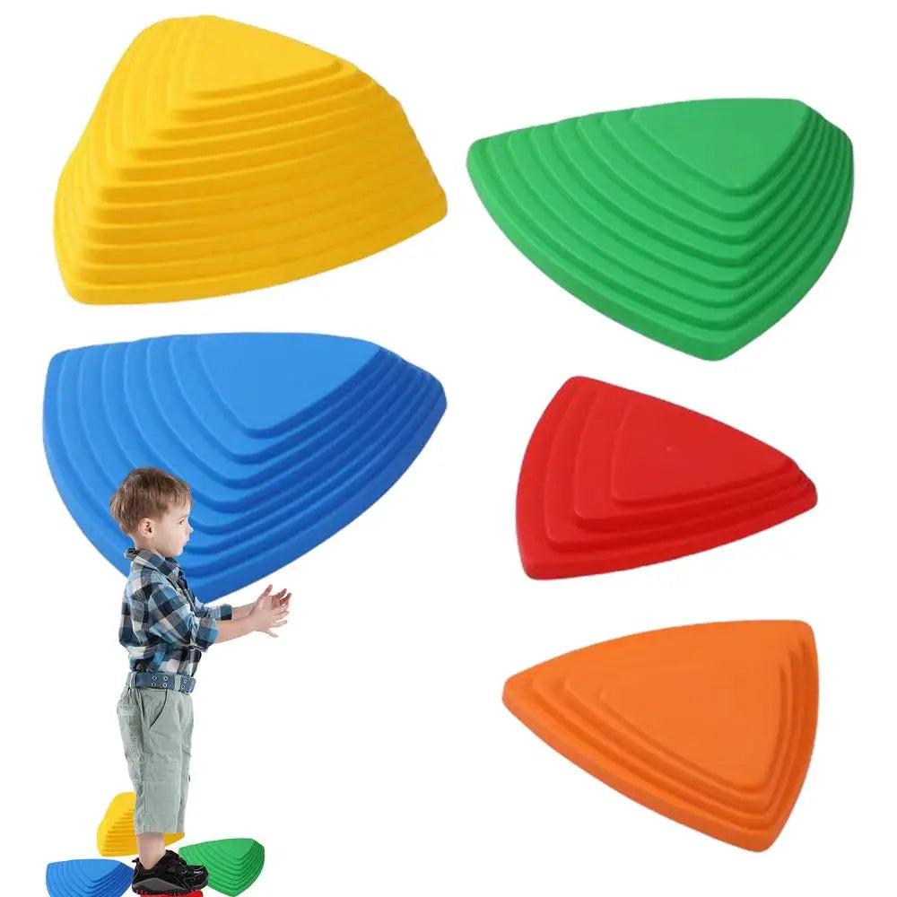 A child stands on a vibrant sensory toy, part of the Kids Balance River Stones set, designed like stepped triangular hills. Nearby are five similar stones in yellow, green, blue, red, and orange.