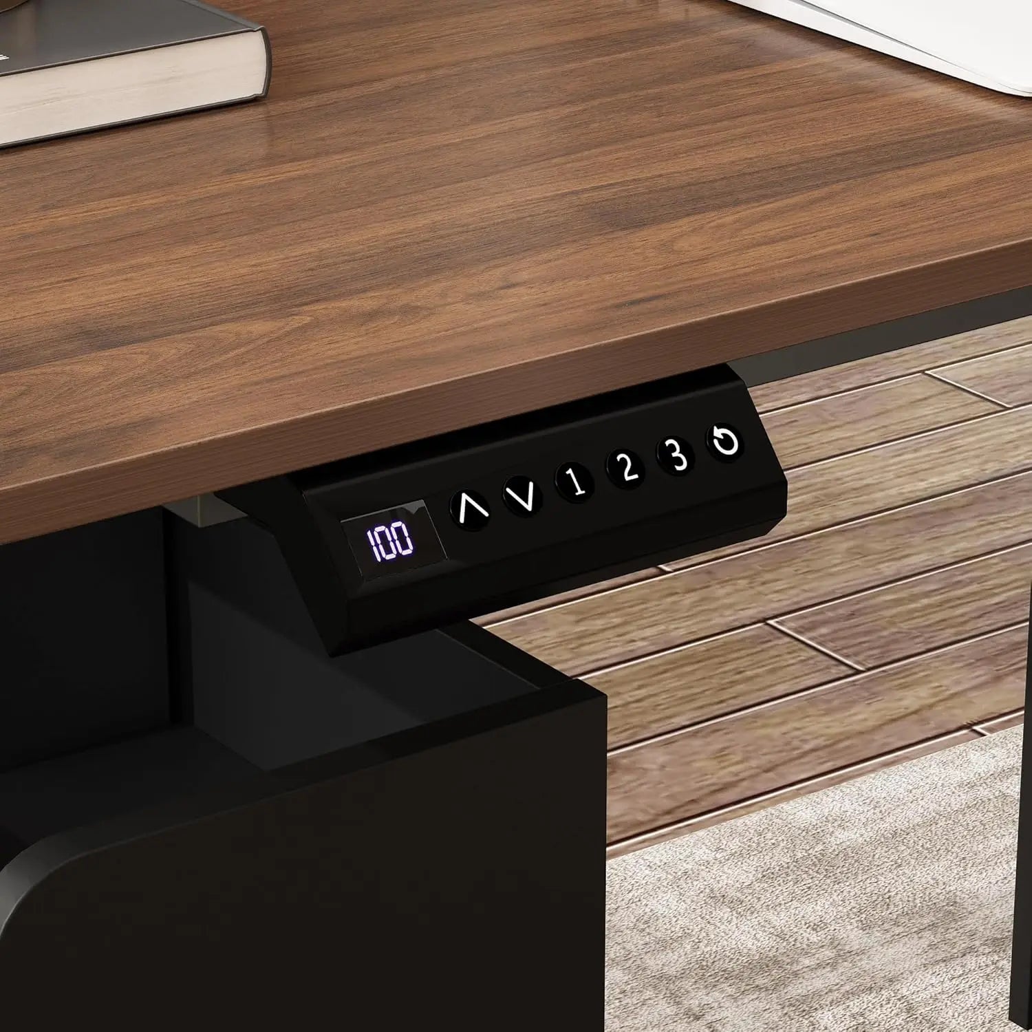 Close-up of the L Shaped Electric Standing Desk with Drawers and Shelves control panel, showing 100 on its digital screen with up/down arrows and numbered buttons, mounted under a wood desktop with an industrial steel frame above a rug and hardwood floor.