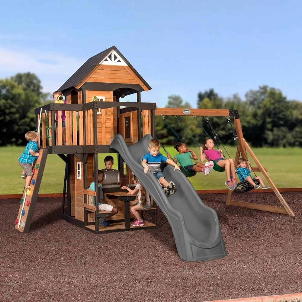 Children enjoy the Playhouse Backyard Discovery Canyon Creek Cedar Swing Set, featuring a slide, swings, climbing wall, and clubhouse. Some swing, one slides, while others climb or play inside the outdoor cedar playground on a sunny day.