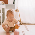 A toddler sits on a rug stacking five colorful, square-shaped Silicone Stacking Cups (Set of 5).