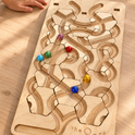 A child’s hand reaches toward The Oort Cloud – Wooden Marble Run Puzzle, which features carved tracks and several colorful glass marbles.