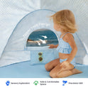 A child in a blue gingham swimsuit sits inside a Kids Beach Tent & Sand Toy Set, opening a zipper vent that reveals a view of the ocean.