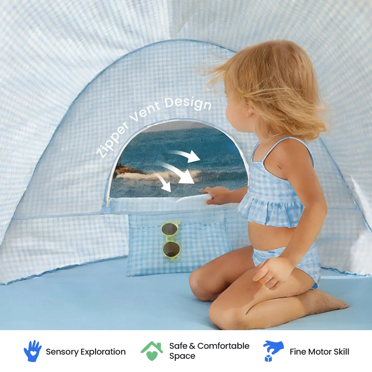 A child in a blue gingham swimsuit sits inside a Kids Beach Tent & Sand Toy Set, opening a zipper vent that reveals a view of the ocean.