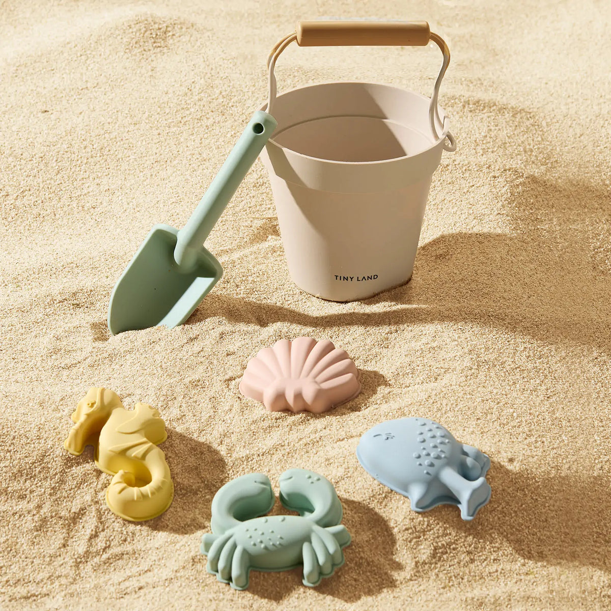 A sand bucket, a shovel, and four sea creature-shaped sand molds from a Kids Beach Tent & Sand Toy Set sitting on the sand.